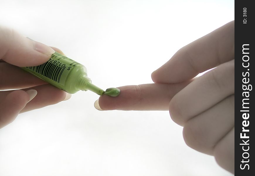 A tube of green liquid eye makeup being squeezed onto index finger. A tube of green liquid eye makeup being squeezed onto index finger