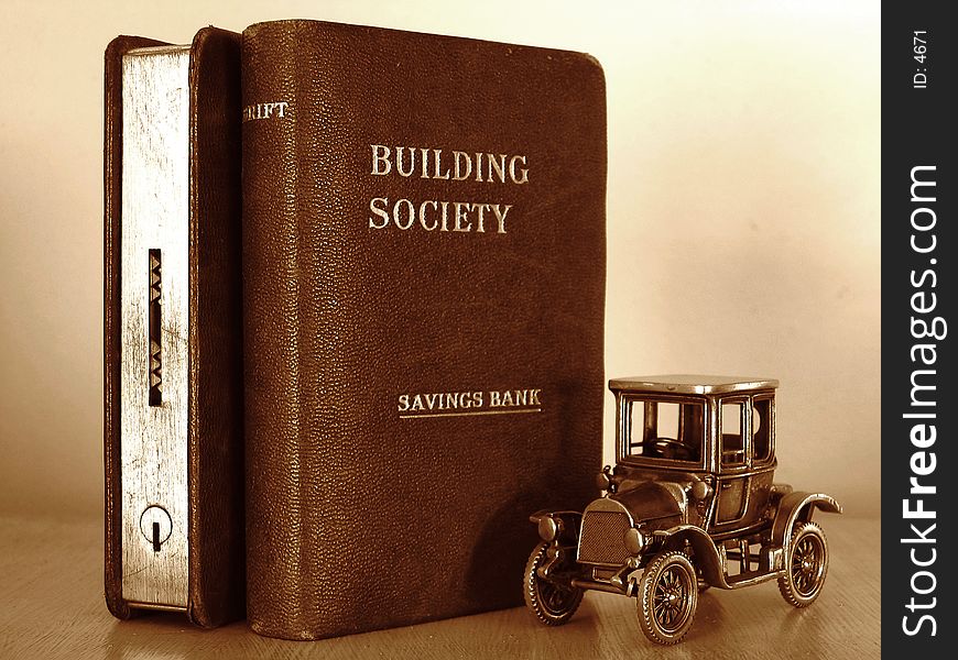 Miniature car standing beside two money boxes in the form of books. Miniature car standing beside two money boxes in the form of books.