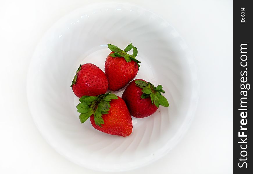 Four delicious looking strawberries sitting in a white bowl. Overhead shot, high key. Four delicious looking strawberries sitting in a white bowl. Overhead shot, high key.