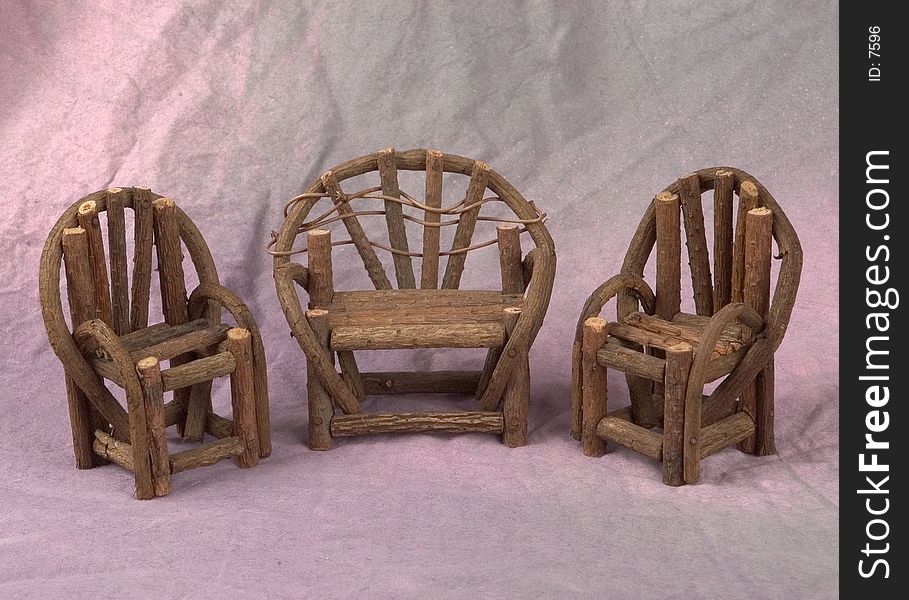 A miniature wooden porch set of a love seat and two chairs photogroaphed on a grey background with pink highlights. A miniature wooden porch set of a love seat and two chairs photogroaphed on a grey background with pink highlights