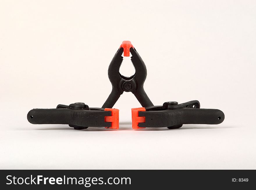 3 spring clips, medium sized, black with orange clamps photographed on a white background