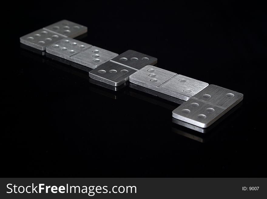 A game of dominoes in progress. Dominoes are metal and on a reflective black background.