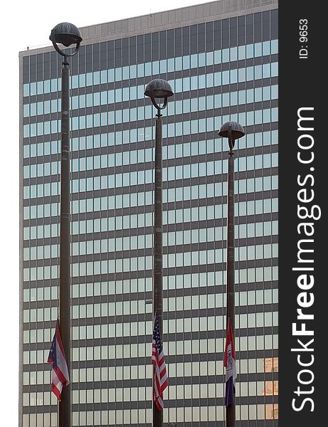 3 flagpoles with the American flag, the Ohio flag, and one othe rflag flying with an office building as the background. 3 flagpoles with the American flag, the Ohio flag, and one othe rflag flying with an office building as the background