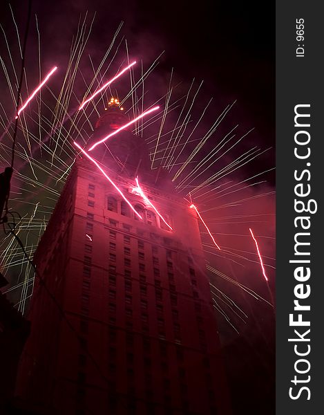 fireworks surround an office building, shooting from behind and crossing in front of the edifice. Walls of the building in front glow red. Fourth of July in America. fireworks surround an office building, shooting from behind and crossing in front of the edifice. Walls of the building in front glow red. Fourth of July in America