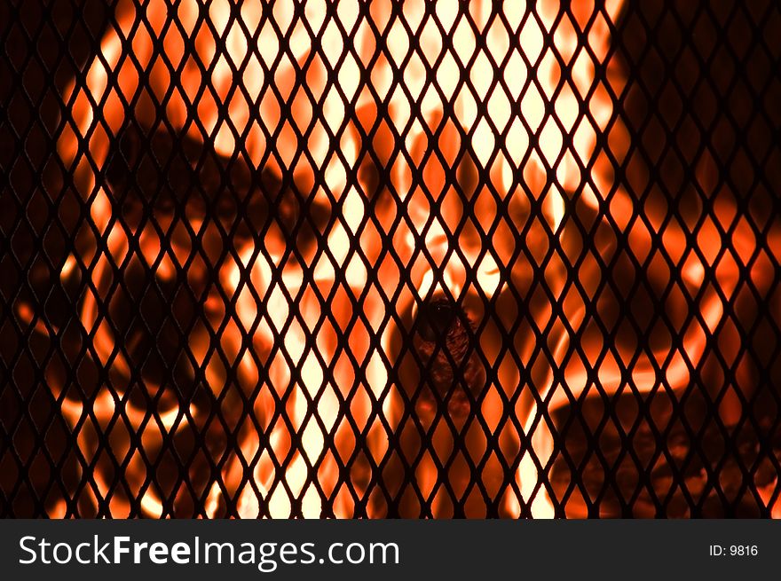 Flames viewed through the grate of the oudoor fireplace. Focus is on grate. Flames viewed through the grate of the oudoor fireplace. Focus is on grate