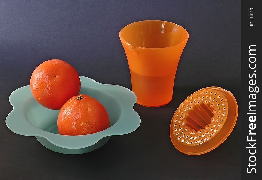 A set with squeezer, two fresh oranges on a blue plastic dish, on a black background. A set with squeezer, two fresh oranges on a blue plastic dish, on a black background