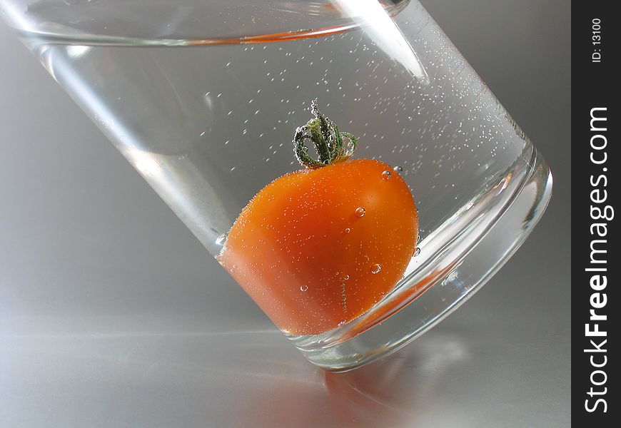 A red tomato in a glass filled with sparkling mineral water. A red tomato in a glass filled with sparkling mineral water.