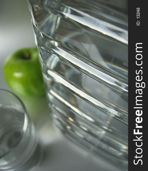 A big water bottle in front of a glass and a green apple. A big water bottle in front of a glass and a green apple.