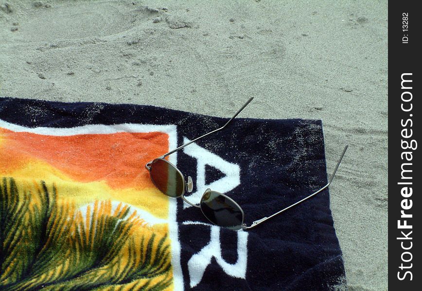 A beach towel, with sunglasses on it, sitting in the sand. A beach towel, with sunglasses on it, sitting in the sand