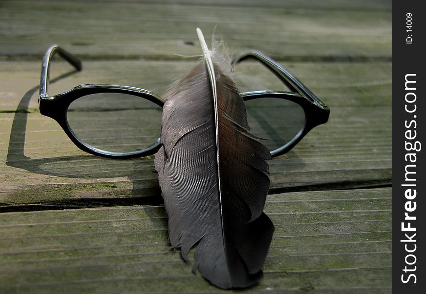 A feather and a sunglass on a wooden table in the forest. A feather and a sunglass on a wooden table in the forest