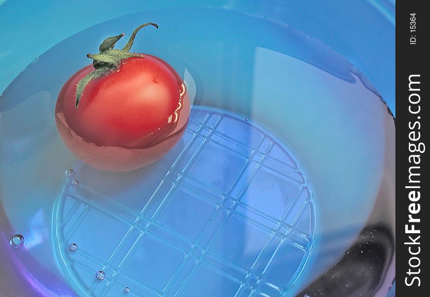 A tomato floating in water in a blue translucent bowl. A tomato floating in water in a blue translucent bowl