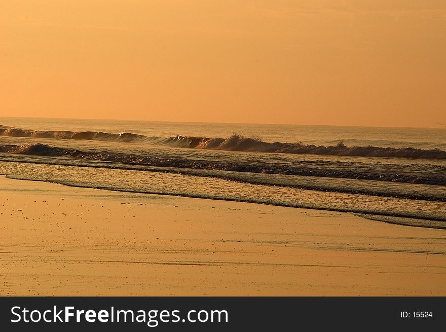 Waves breaking on the beach are turned a light shade of orange from the rising sun. Emerald Isle, North Carolina. Waves breaking on the beach are turned a light shade of orange from the rising sun. Emerald Isle, North Carolina