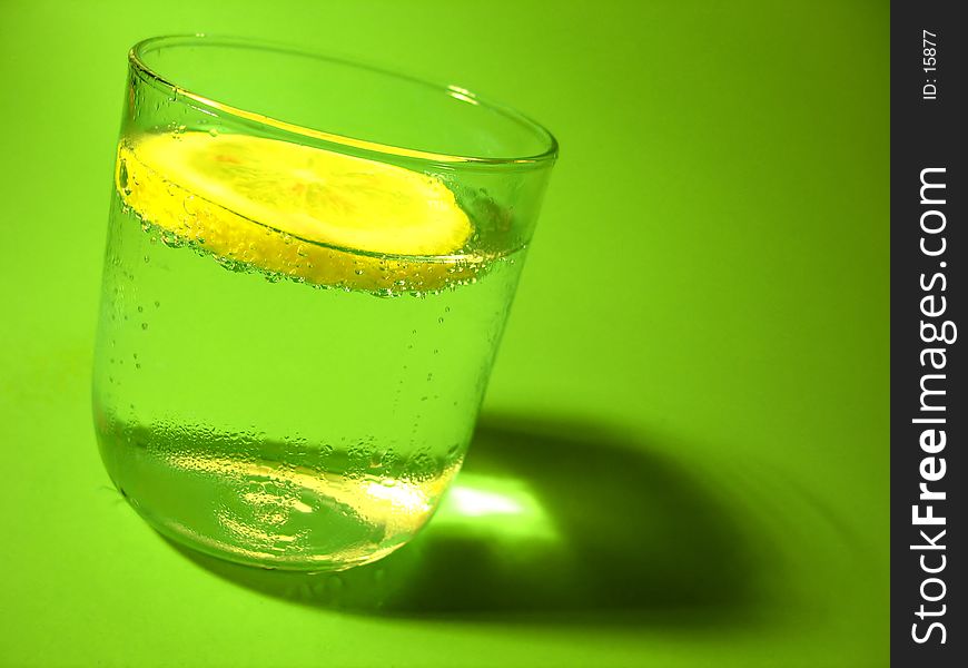 A glass of carbonated water with a lemon slice and vibrant green background. A glass of carbonated water with a lemon slice and vibrant green background.