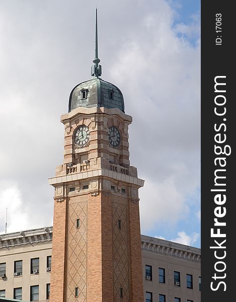 Clock tower standing in front of a cloudy sky with a shortter building in the background