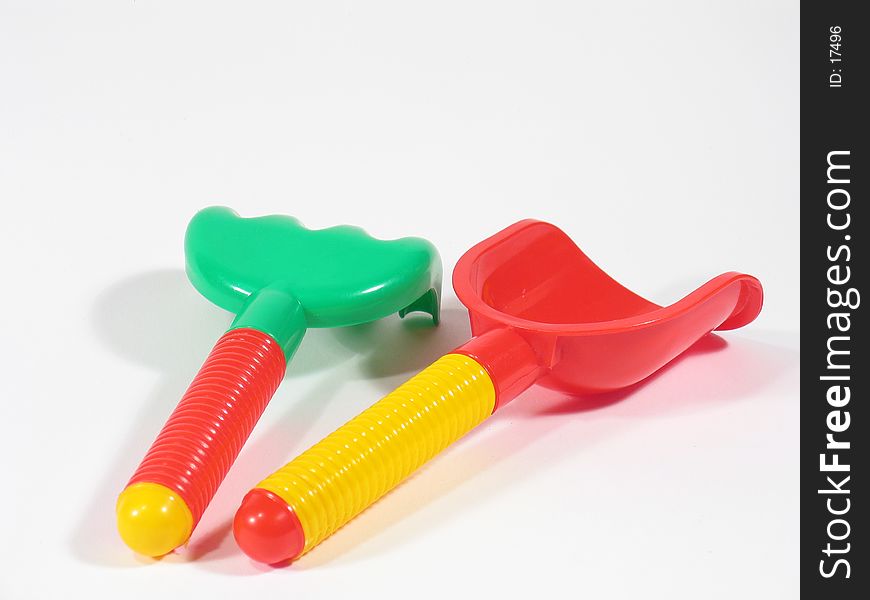 A green and red sandbox toy rake and a red and yellow toy shovel. A green and red sandbox toy rake and a red and yellow toy shovel.