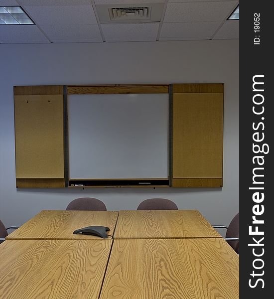 A straight on view of a conference table, with conference phone in the middle, chairs, and a blank whiteboard. Crop is vertical. A straight on view of a conference table, with conference phone in the middle, chairs, and a blank whiteboard. Crop is vertical