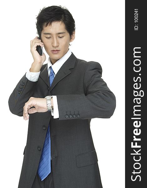 An asian businessman checks the time whist taking on the telephone. An asian businessman checks the time whist taking on the telephone