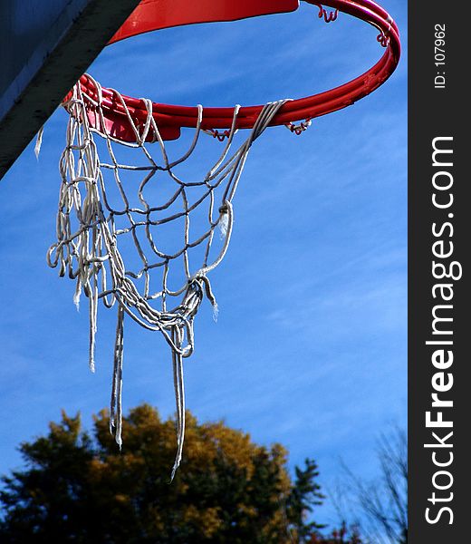 Orange basketball hoop with white tattered strings set off against a rich blue sky, trees in the background, easthampton, massachusetts. Orange basketball hoop with white tattered strings set off against a rich blue sky, trees in the background, easthampton, massachusetts