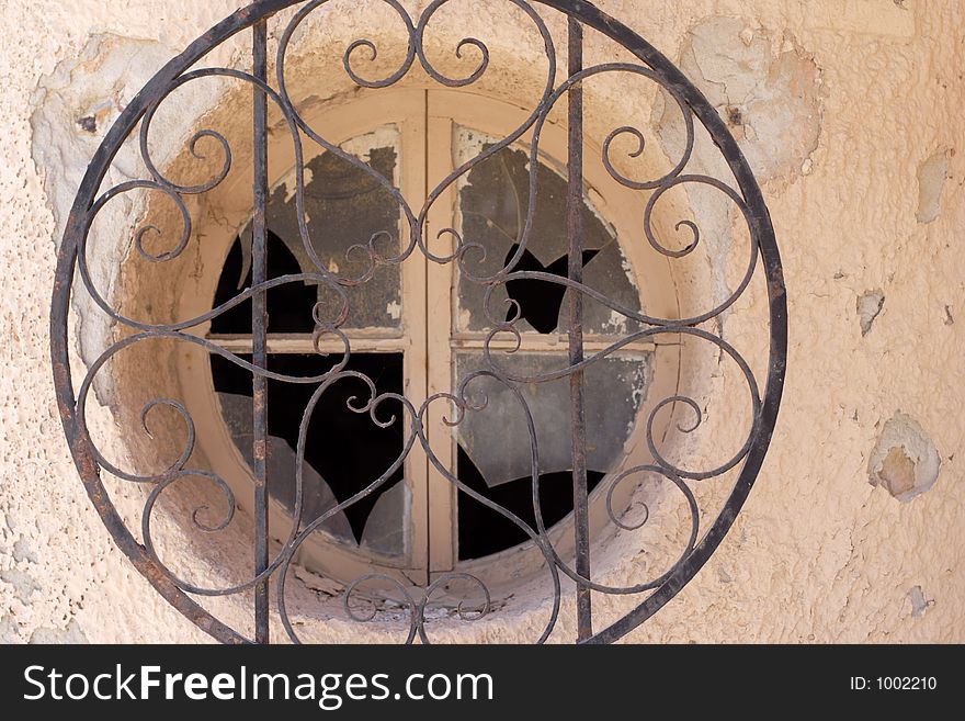 Old smashed circlular window with iron grate covering. Old smashed circlular window with iron grate covering