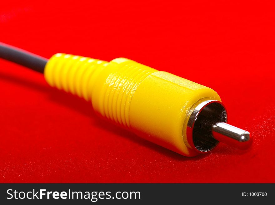 Closeup of an RCA-style (yellow) video cable against a bright red background. Closeup of an RCA-style (yellow) video cable against a bright red background