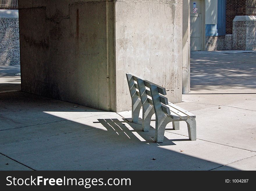 Concrete bench sitting in the shadows of the archway from a large building. Concrete bench sitting in the shadows of the archway from a large building.