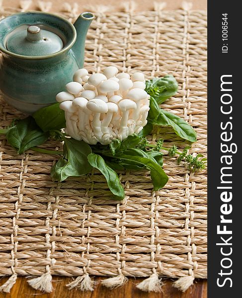 Fresh enoki mushrooms on a bed of basil with a soy sauce pitcher in the background suggesting asian type cooking and healthy eating.  Focus in on mushrooms and basil.