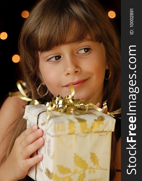 A cute young girl holding a christmas gift, dark background with christmas light bokeh. A cute young girl holding a christmas gift, dark background with christmas light bokeh