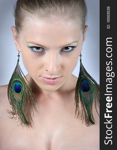 Close-up young blonde model with peacock earrings posing with beautiful make-up. Close-up young blonde model with peacock earrings posing with beautiful make-up