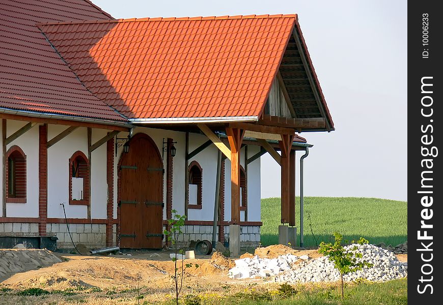 A view of new white farmhouse with big gate and red roof. Pieces of bricks in the front of the farmhouse.