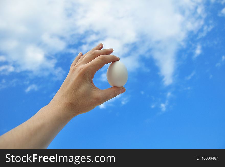 Egg in a hand against the blue sky