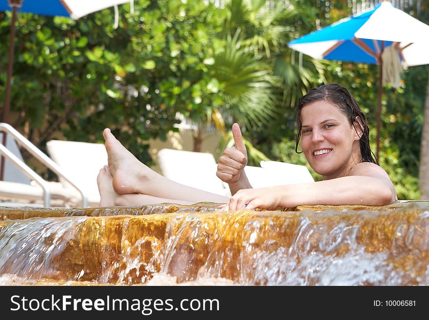 Young woman in a beautiful pool with palms in the background. She is showing a thumbs up sign. Young woman in a beautiful pool with palms in the background. She is showing a thumbs up sign.