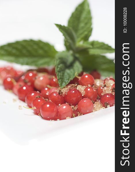 Bright red translucent edible Redcurrant berries with cane sugar and lemon balm on white plate at white background