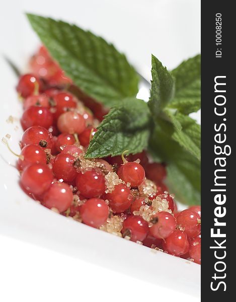 Bright red translucent edible Redcurrant berries with cane sugar and lemon balm on white plate at white background