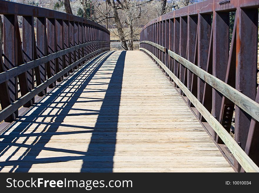 Walkway bridge with wooden footpath and steel trusses, located in a city park.