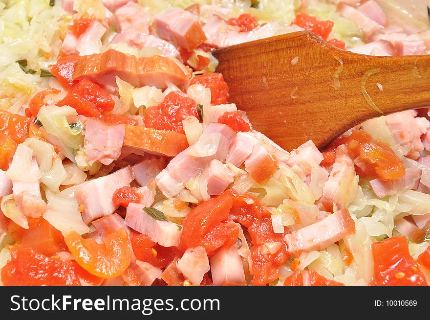 Cooking cabbage with ham an tomato in a pan