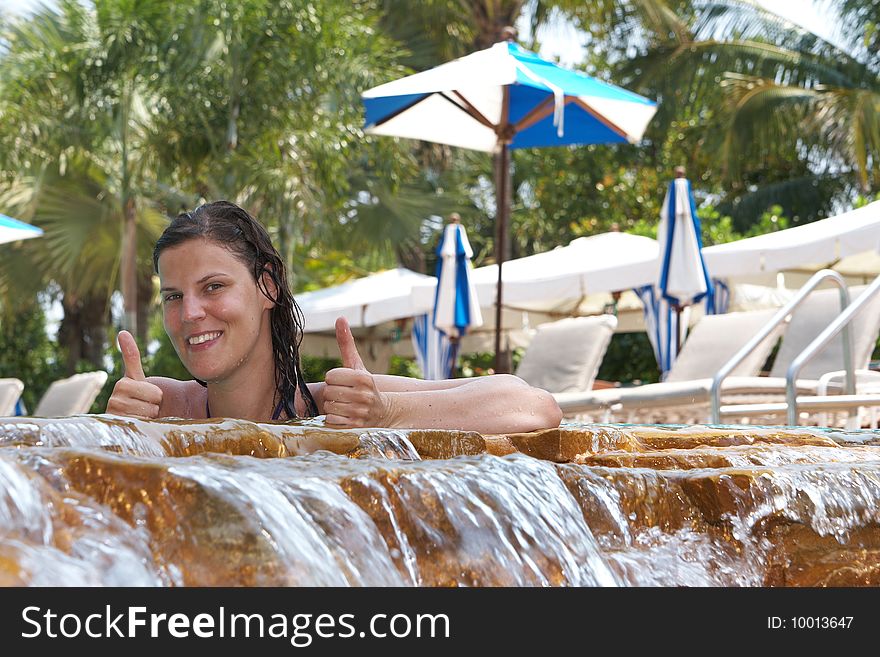 Young woman in a beautiful pool with palms in the background. She is showing a thumbs up sign. Young woman in a beautiful pool with palms in the background. She is showing a thumbs up sign.