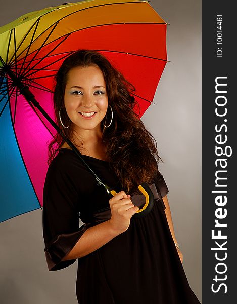 Beautiful girl with many-colored umbrella on the grey background