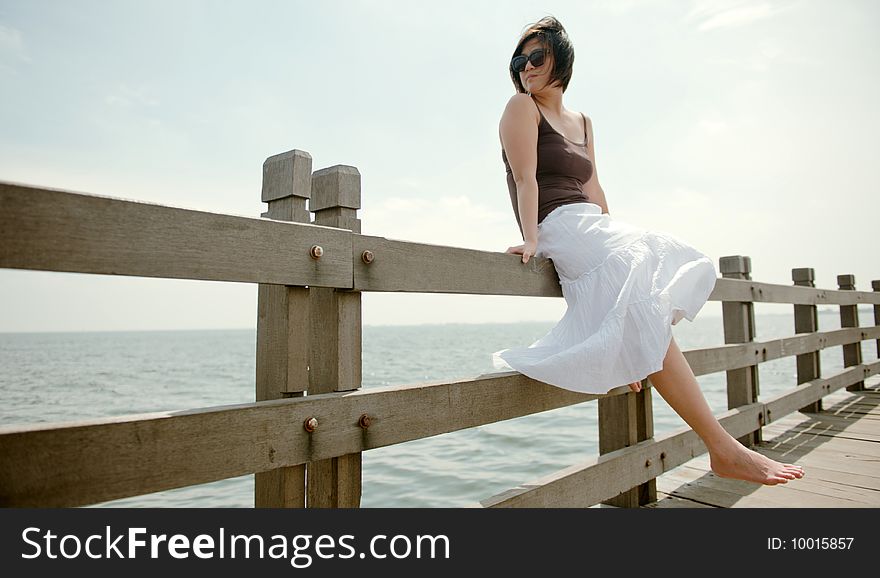 An Asian girl sits on a railing at the seaside. An Asian girl sits on a railing at the seaside.