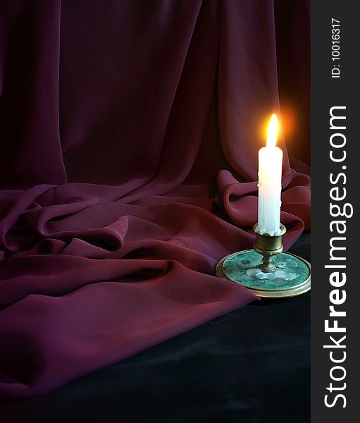 Burning candle and fabric against a dark background.