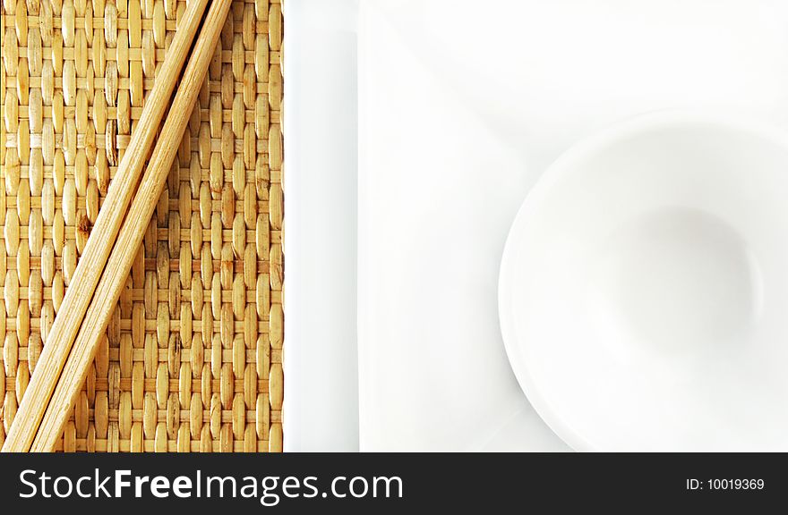 White dishes and wooden chopsticks on a bamboo mat. White dishes and wooden chopsticks on a bamboo mat.