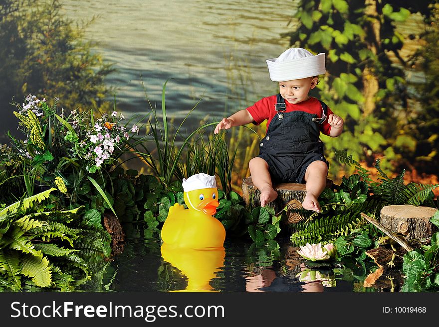 A barefoot baby boy in a sailor's hat playing with a rubber duck in a sailor's hat by the water's edge. A barefoot baby boy in a sailor's hat playing with a rubber duck in a sailor's hat by the water's edge.