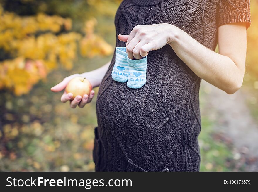 Beautiful portrait of pregnant woman with booties on her tummy in the September colorful autumn forest. The concept of pregnancy and the seasons. Beautiful portrait of pregnant woman with booties on her tummy in the September colorful autumn forest. The concept of pregnancy and the seasons