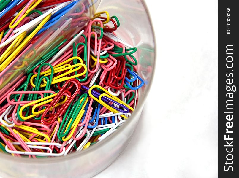 A clear cup is filled is brightly colored paperclips on a white background. A clear cup is filled is brightly colored paperclips on a white background.