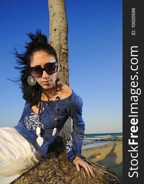 Portrait of young woman on the beach leaning against palm tree trunk. Portrait of young woman on the beach leaning against palm tree trunk