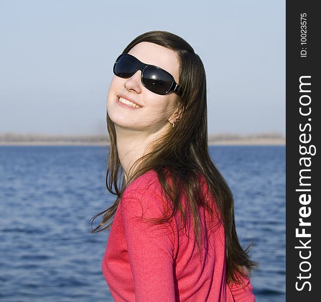 Closeup portrait of a beautiful young woman in sunglasses over big blue sky