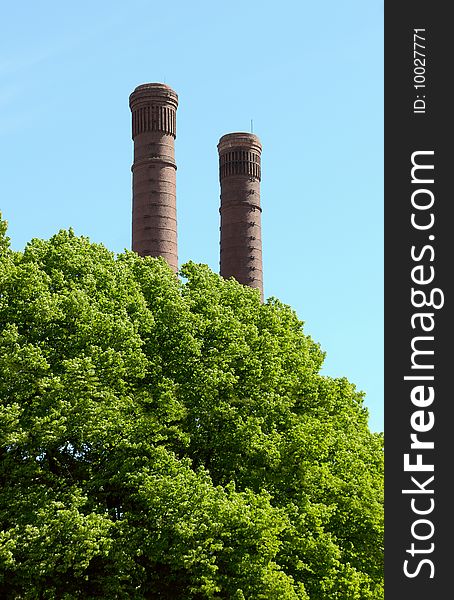 Old factory pipes and green trees against the blue sky. Old factory pipes and green trees against the blue sky.