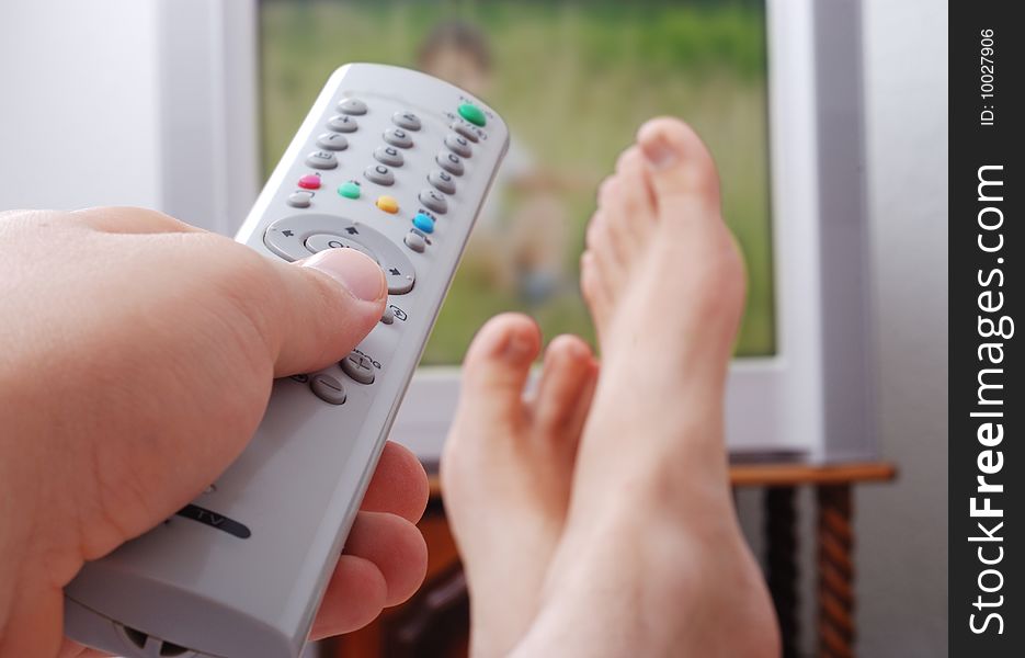 Remote control used by adult man in his hand and the legs are on the table. Remote control used by adult man in his hand and the legs are on the table