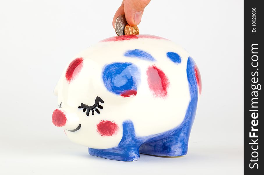 Fingers add coins to a piggy bank; isolated on a white background. Fingers add coins to a piggy bank; isolated on a white background.