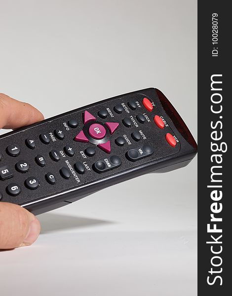 A person's hand holds a television remote control; isolated a gray background.