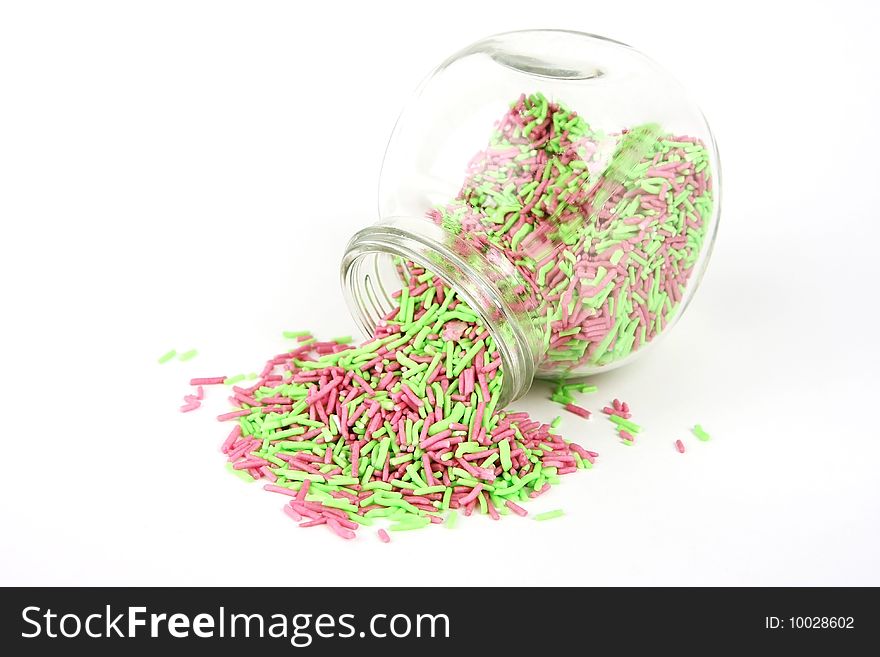 Pink and green sprinkles coming out of a small container on a white background. Pink and green sprinkles coming out of a small container on a white background